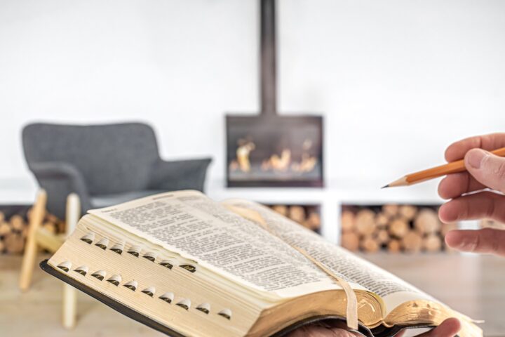 A man holding a Bible with a pencil, against the background of the living room.