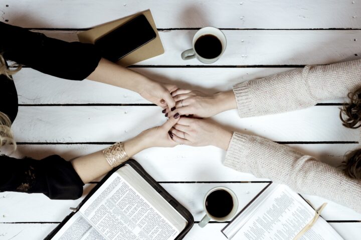 Overhead shot of females holding hands over the table with coffees and open bibles